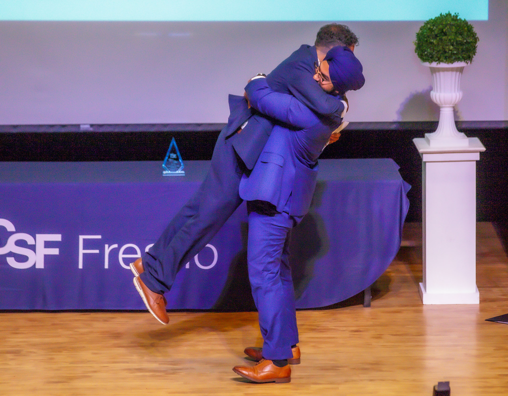 Two graduates hug in celebration on stage