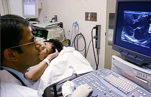 patient in bed in background, while medical specialist looks at ultrasound machine