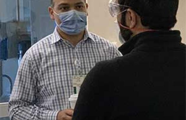 two men wearing face masks appear engaged in conversation