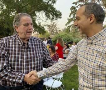 Patient Nat DiBuduo thanking Dr. Mohamed Fayed at a social gathering on the grass surrounded by trees.